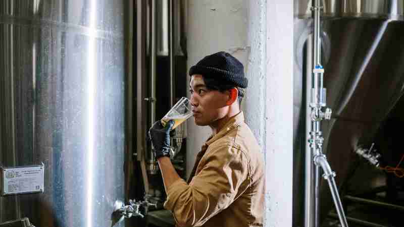 Asian man sampling craft beer in a modern brewery setting., tags: die - pexel