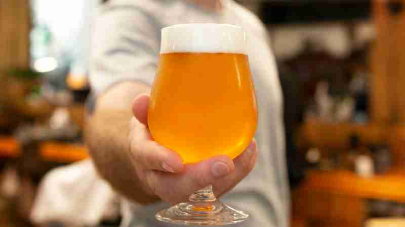 A detailed view of a hand presenting a frothy glass of lager beer in a cozy setting., tags: bier - pexel